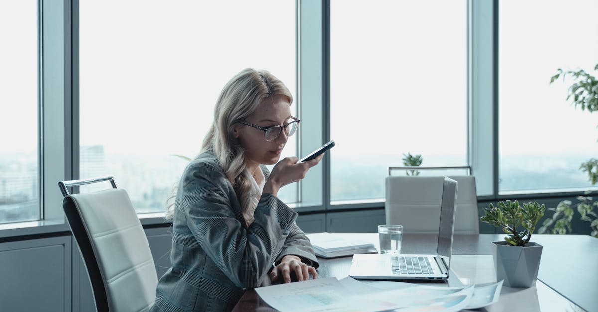 Businesswoman using phone in modern office with laptop and documents.